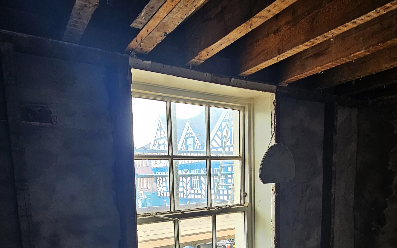 Exposed roof timbers and a sash window looking out over Warwick's historic town centre, mid-way through refurbishment works